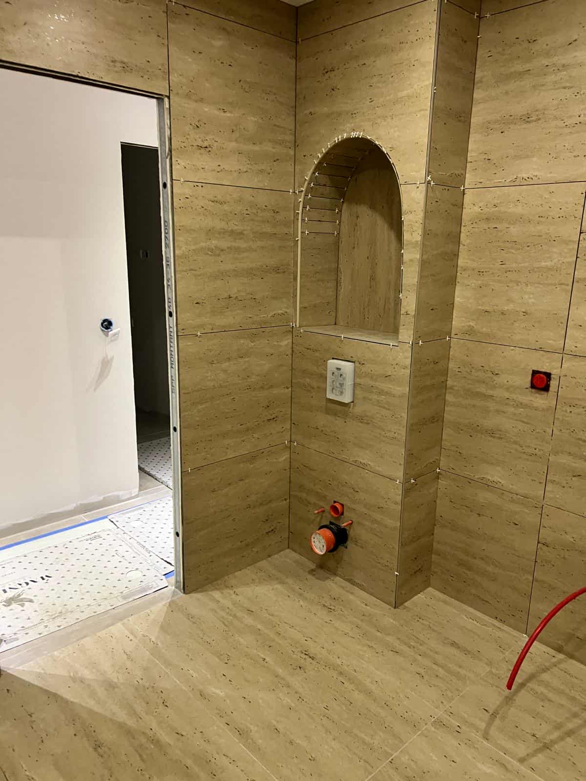 Pose de carrelage travertin dans une salle de bain avec niche arrondie